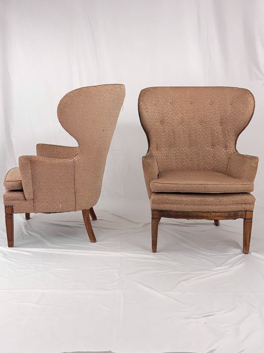 Two wingback chairs with blush colored upholstery on a white background