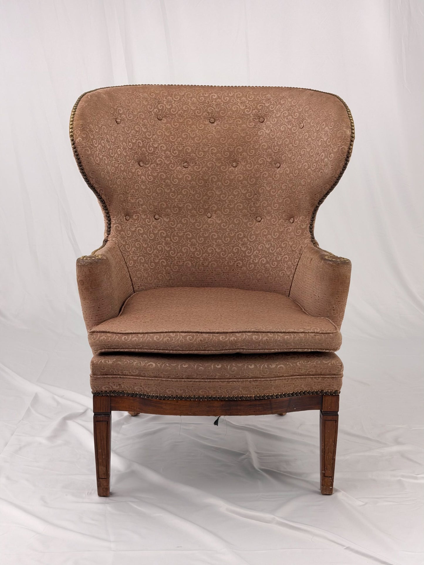 A wingback chair with blush colored upholstery on a white background