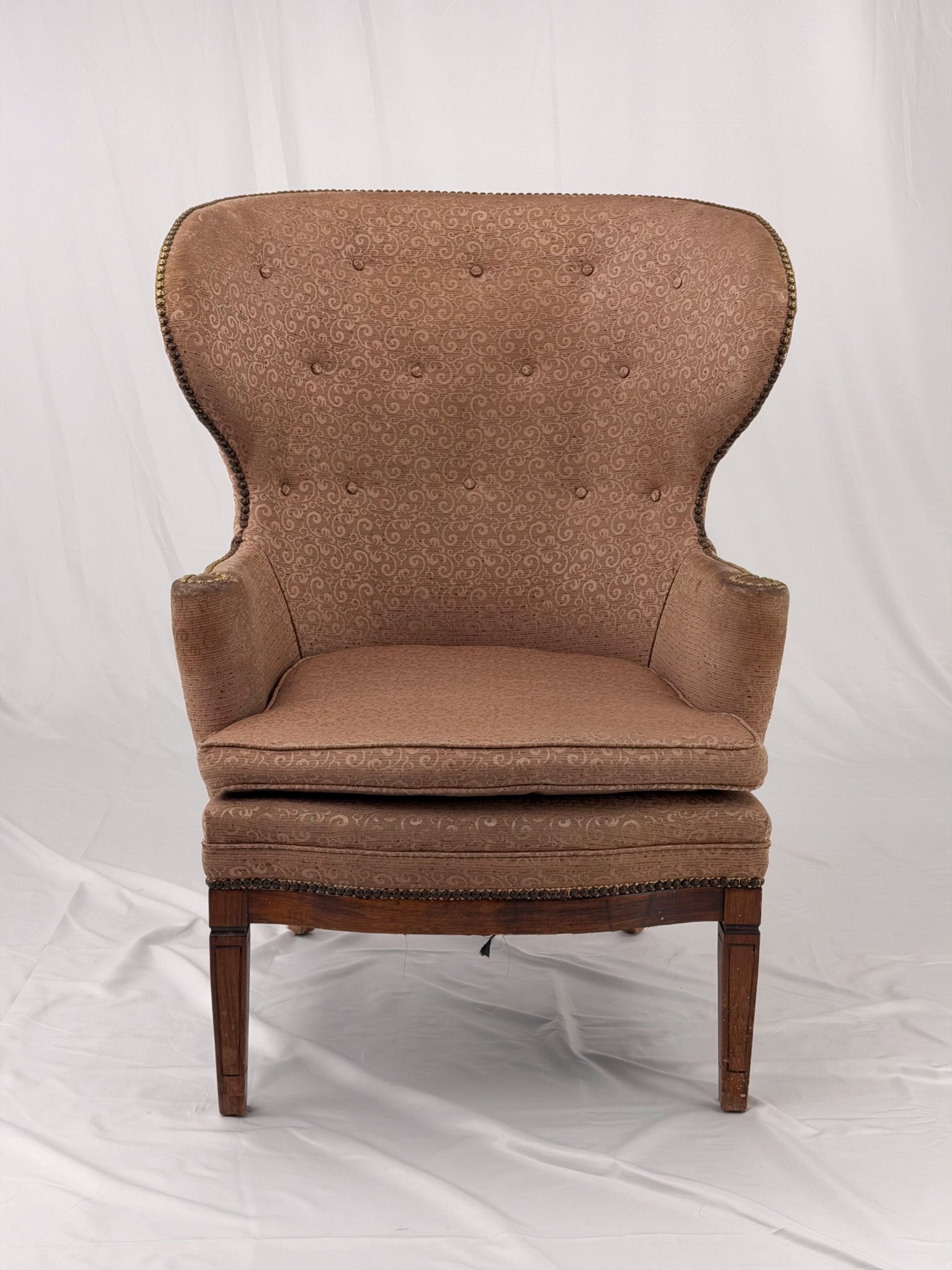 A wingback chair with blush colored upholstery on a white background