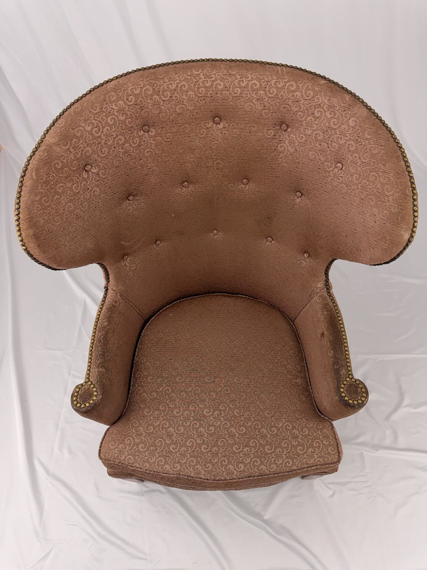 A wingback chair with blush colored upholstery on a white background