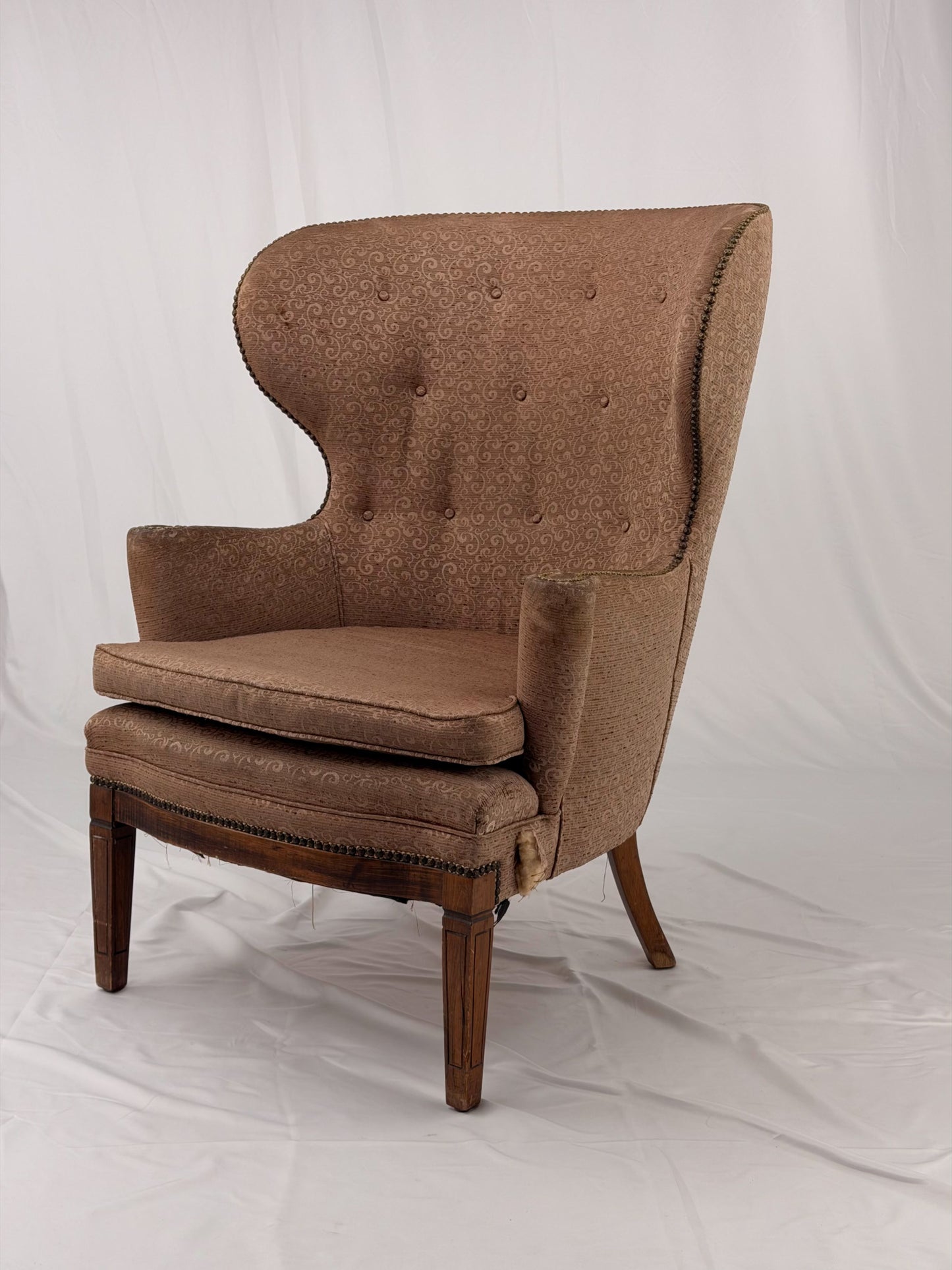 A wingback chair with blush colored upholstery on a white background
