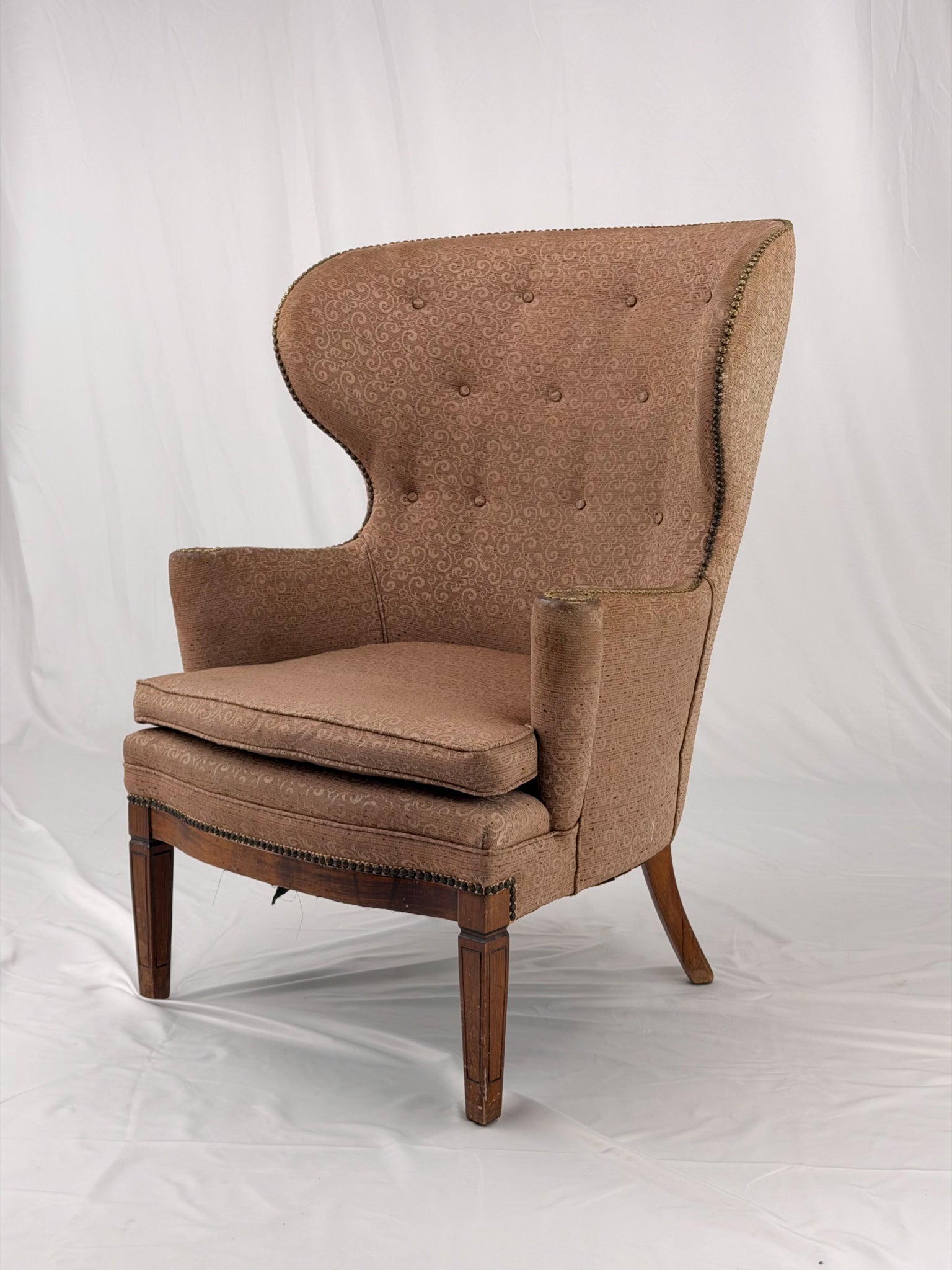 A wingback chair with blush colored upholstery on a white background
