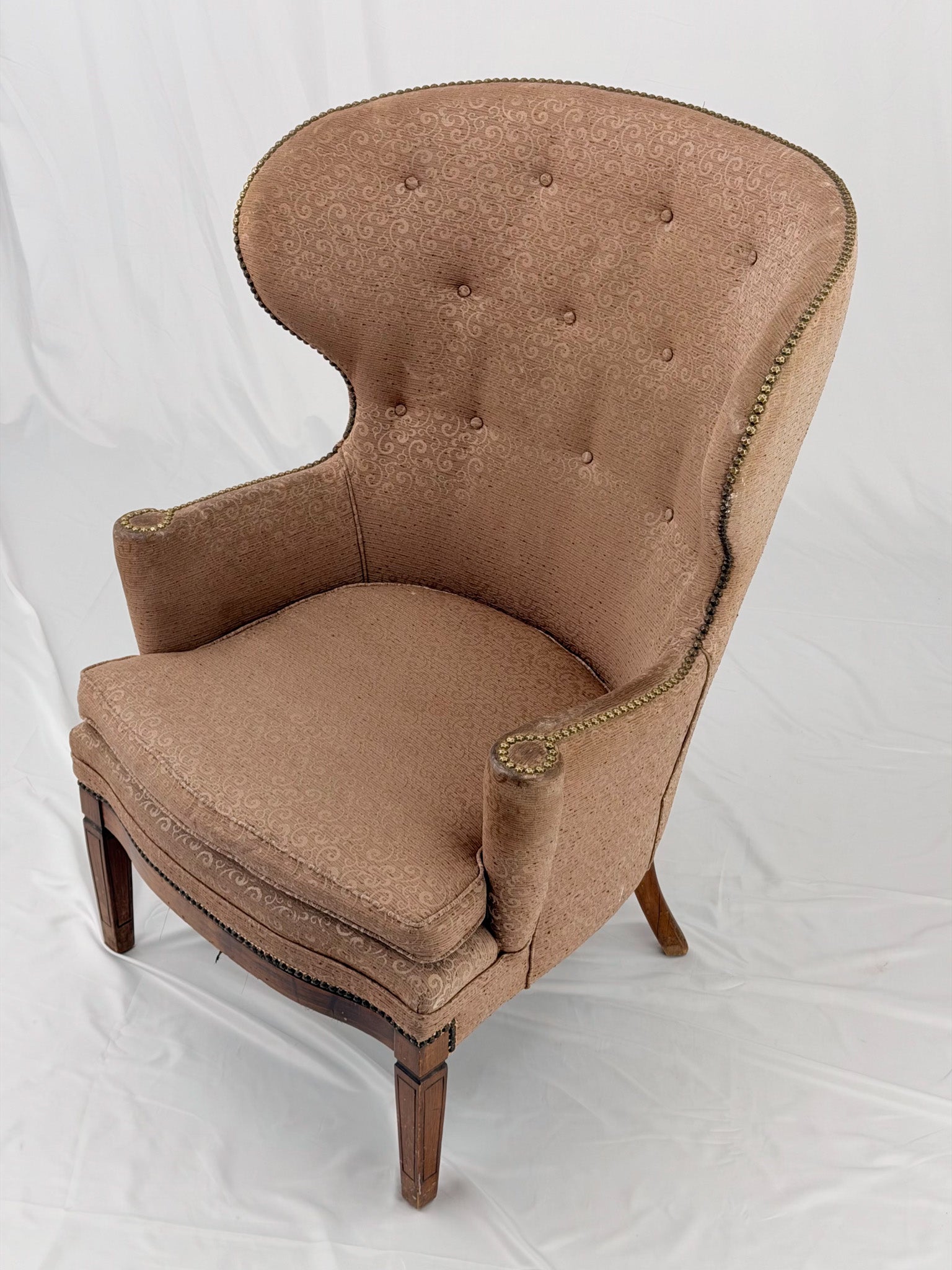 A wingback chair with blush colored upholstery on a white background