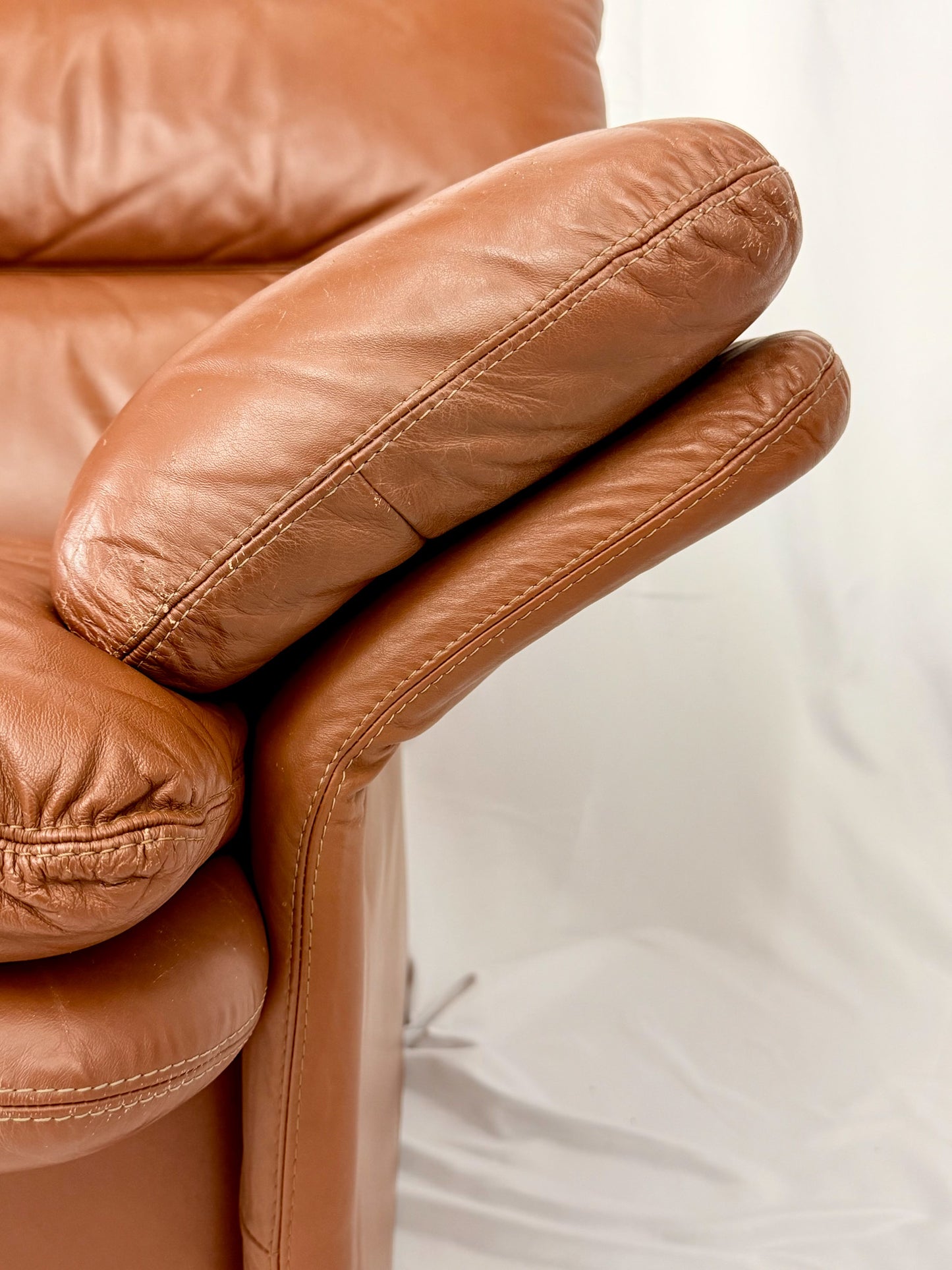 Close-up of a brown leather sofa with a blurred white background