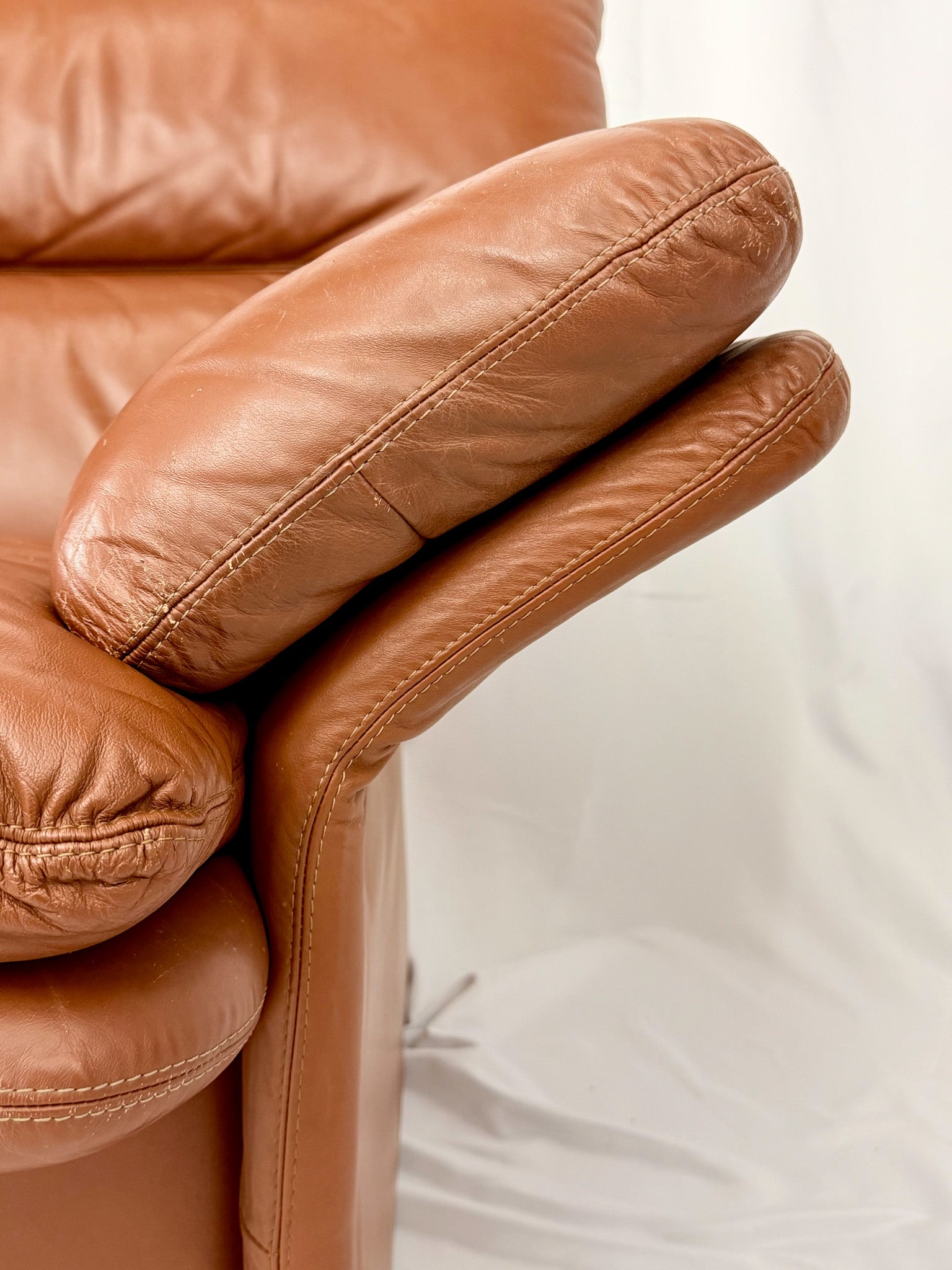 Close-up of a brown leather sofa with a blurred white background