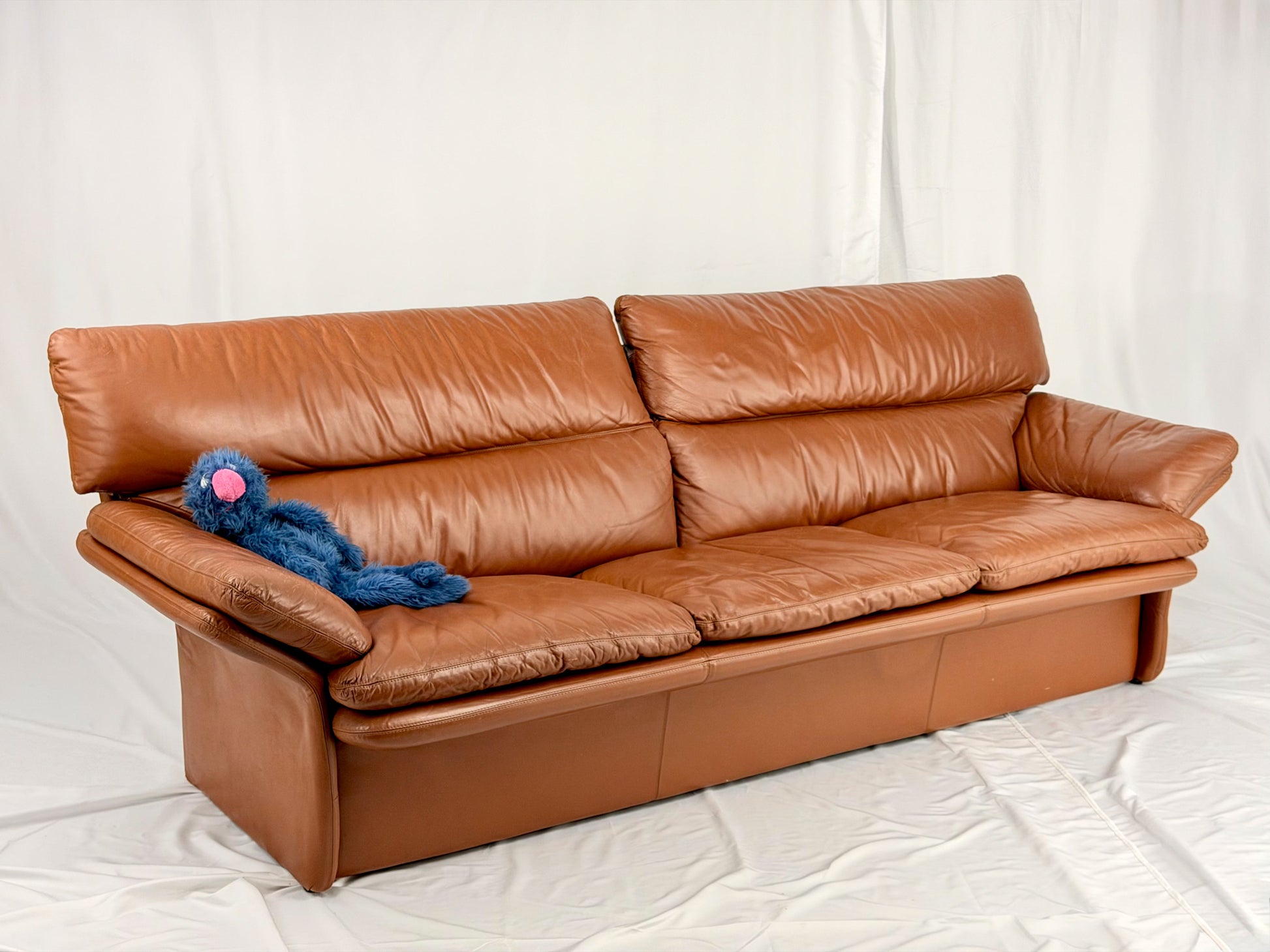 Brown leather sofa with a blue plush toy on a white background