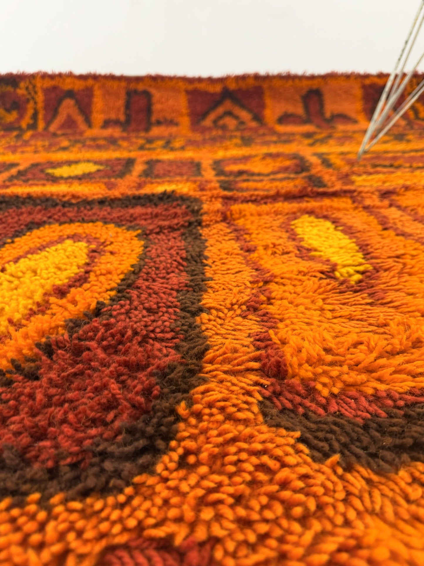 Close up of a Rya shag rug with warm toned geometric pattern on a white background