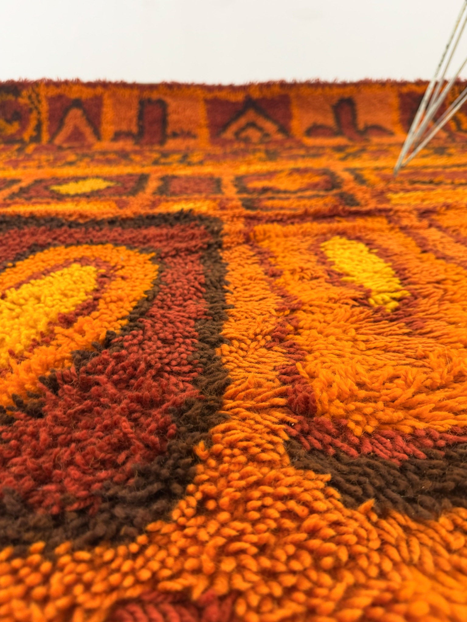Close up of a Rya shag rug with warm toned geometric pattern on a white background