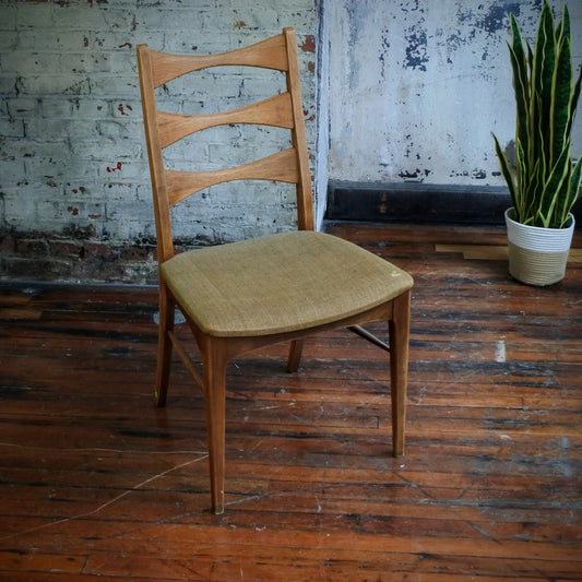 Wooden chair with a beige cushion on a wooden floor against a textured wall.