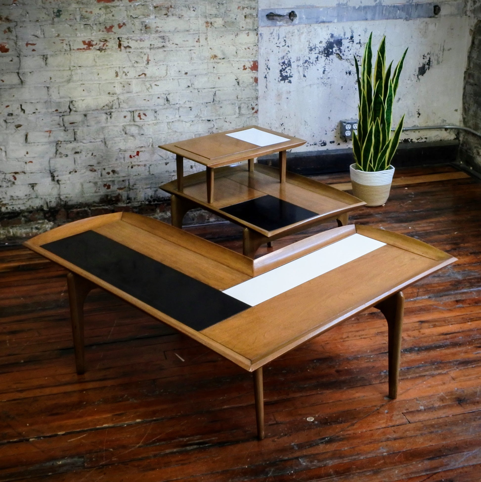Wooden boomerang coffee table with tile top on a wooden floor with a plant in the background.