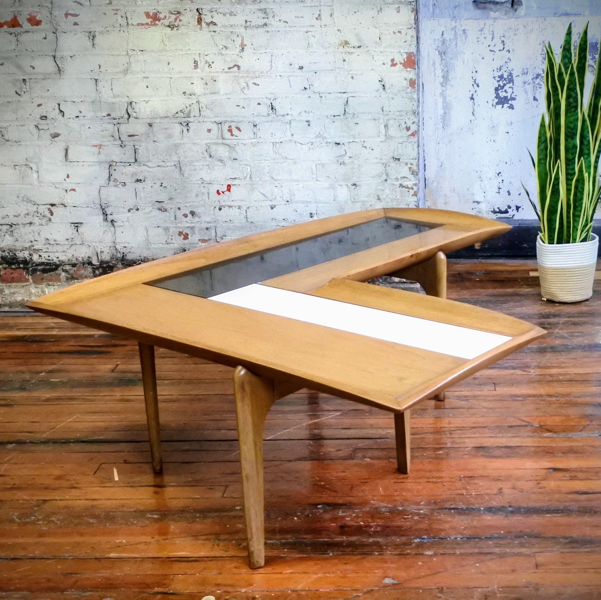 Wooden boomerang coffee table with tile top on a wooden floor with a plant in the background.