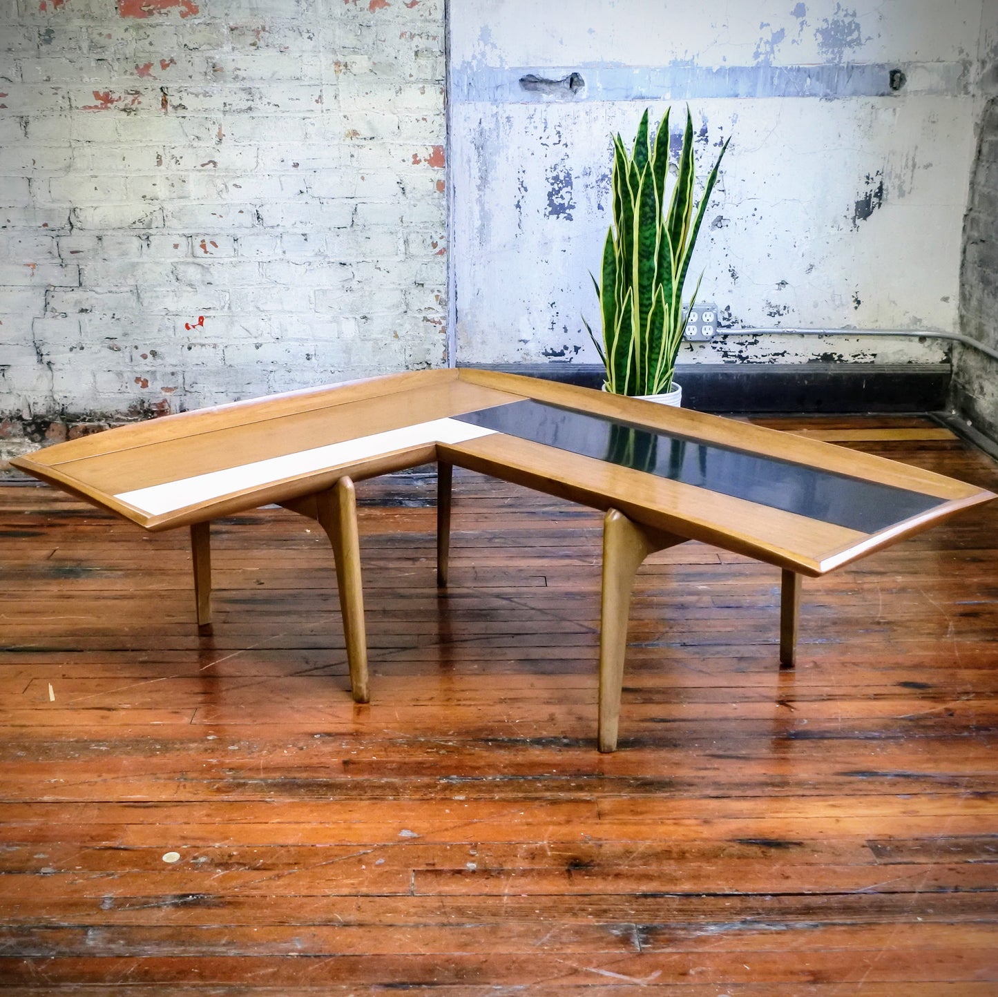 Wooden boomerang coffee table with tile top on a wooden floor with a plant in the background.