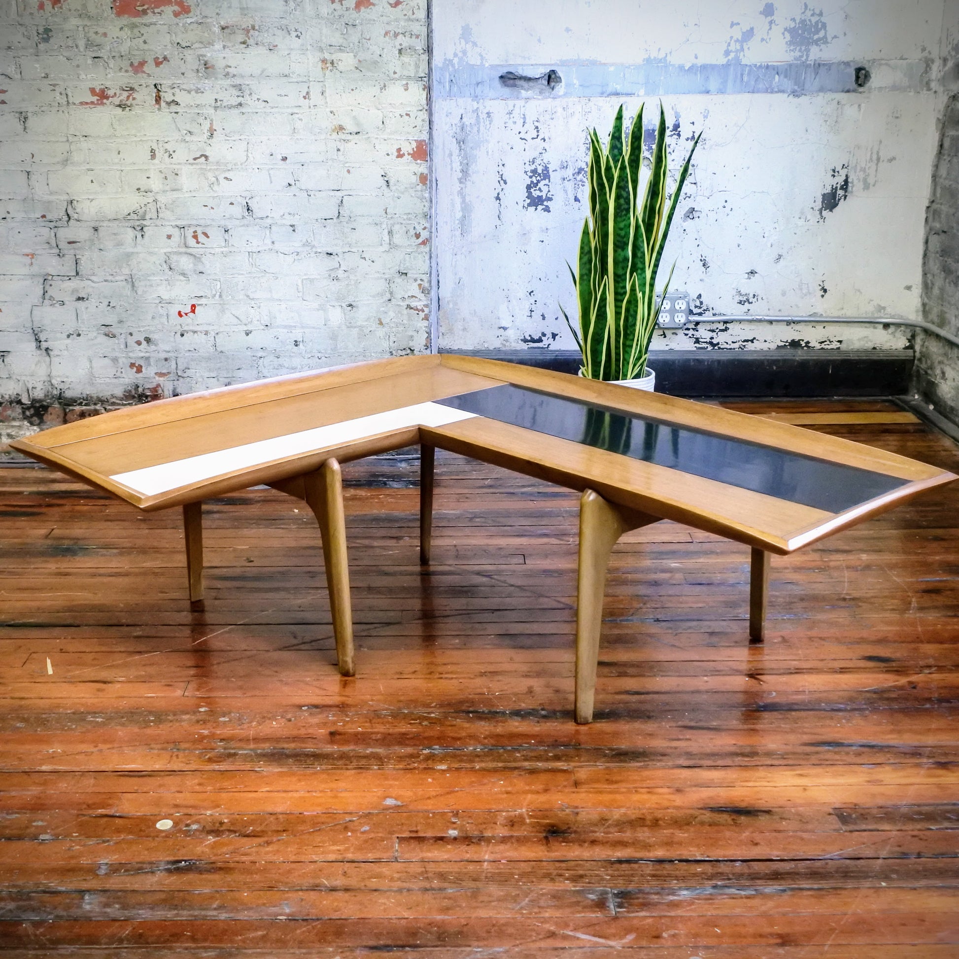 Wooden boomerang coffee table with tile top on a wooden floor with a plant in the background.