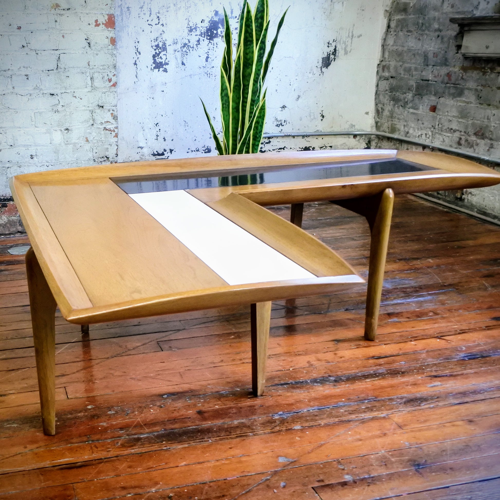 Wooden boomerang coffee table with tile top on a wooden floor with a plant in the background.