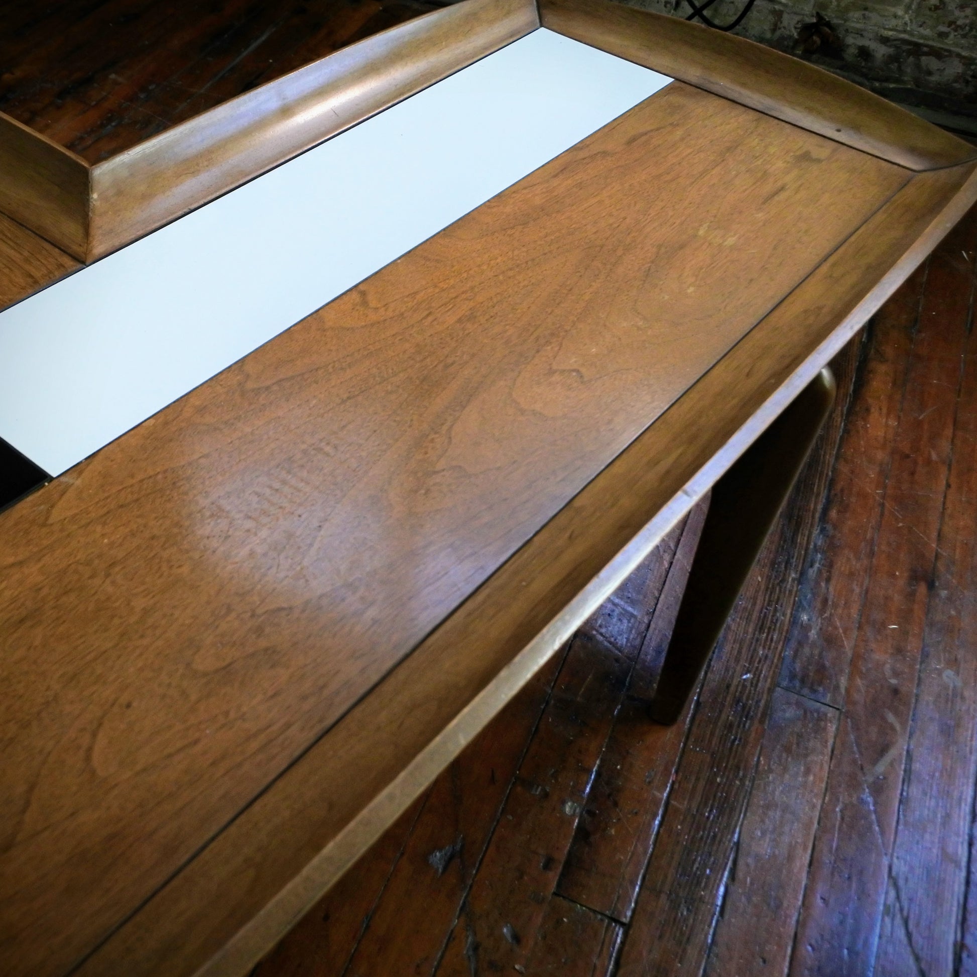 Wooden boomerang coffee table with tile top on a wooden floor with a plant in the background.