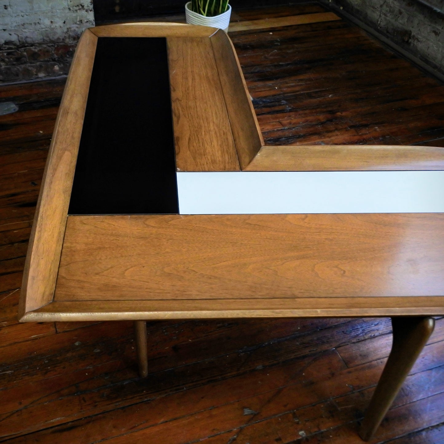 Wooden boomerang coffee table with tile top on a wooden floor with a plant in the background.