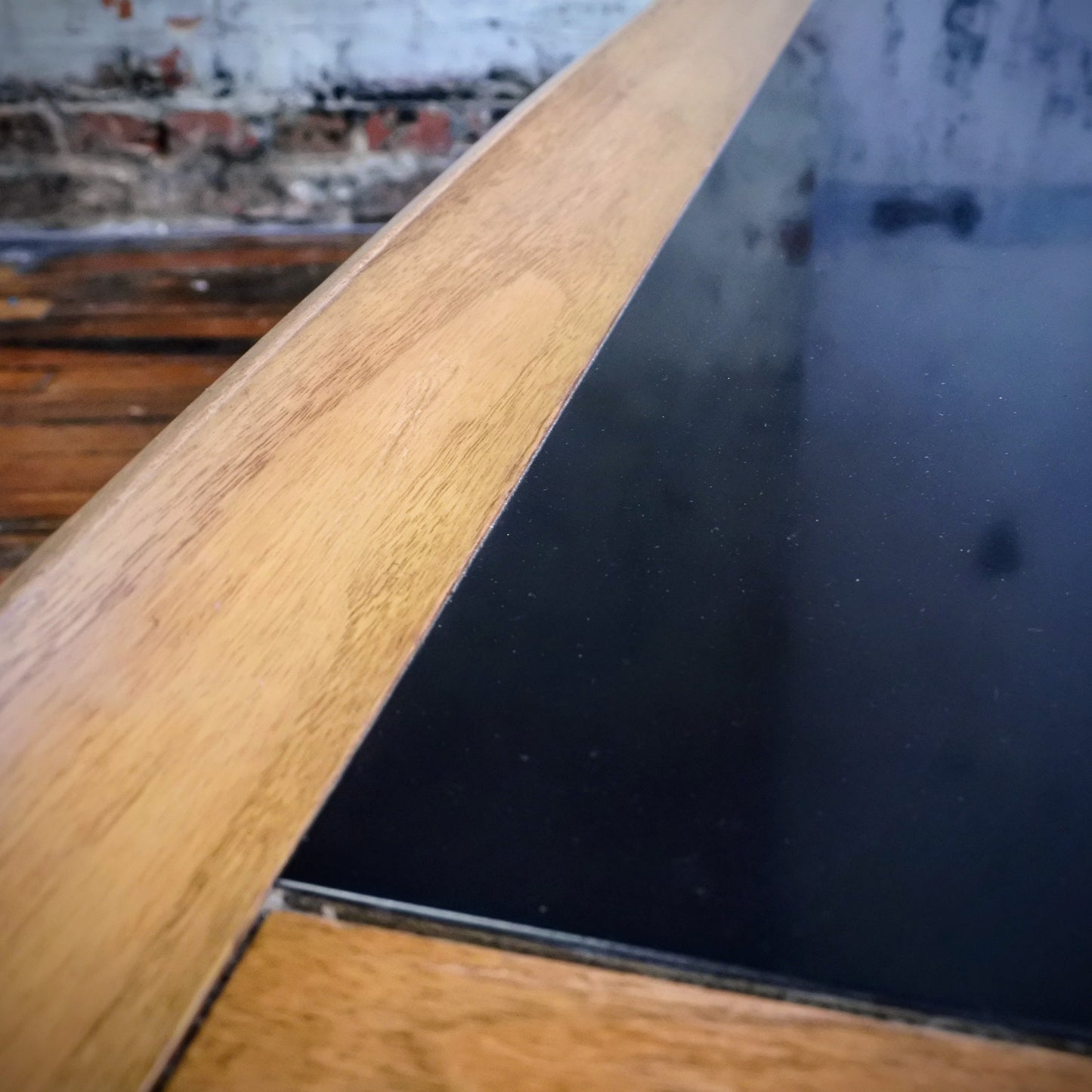 Wooden boomerang coffee table with tile top on a wooden floor with a plant in the background.