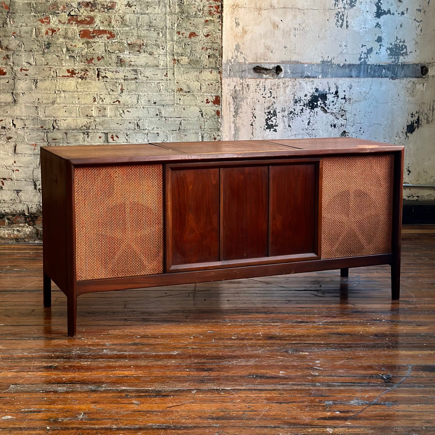 Wooden audio console with vintage design against a textured wall.