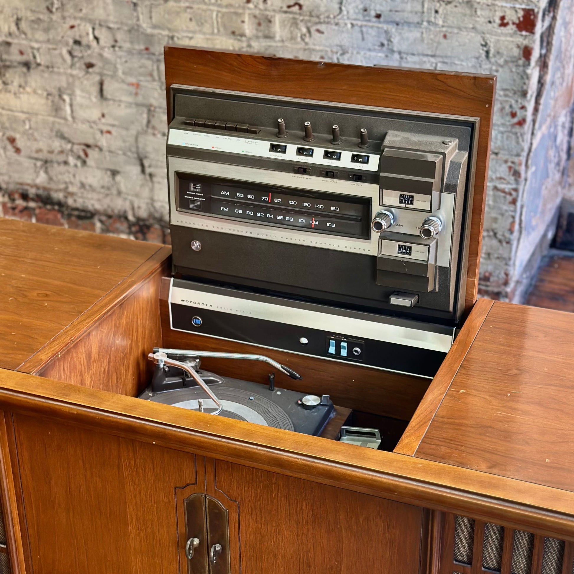 Wooden console with vintage radio against a rustic brick wall.