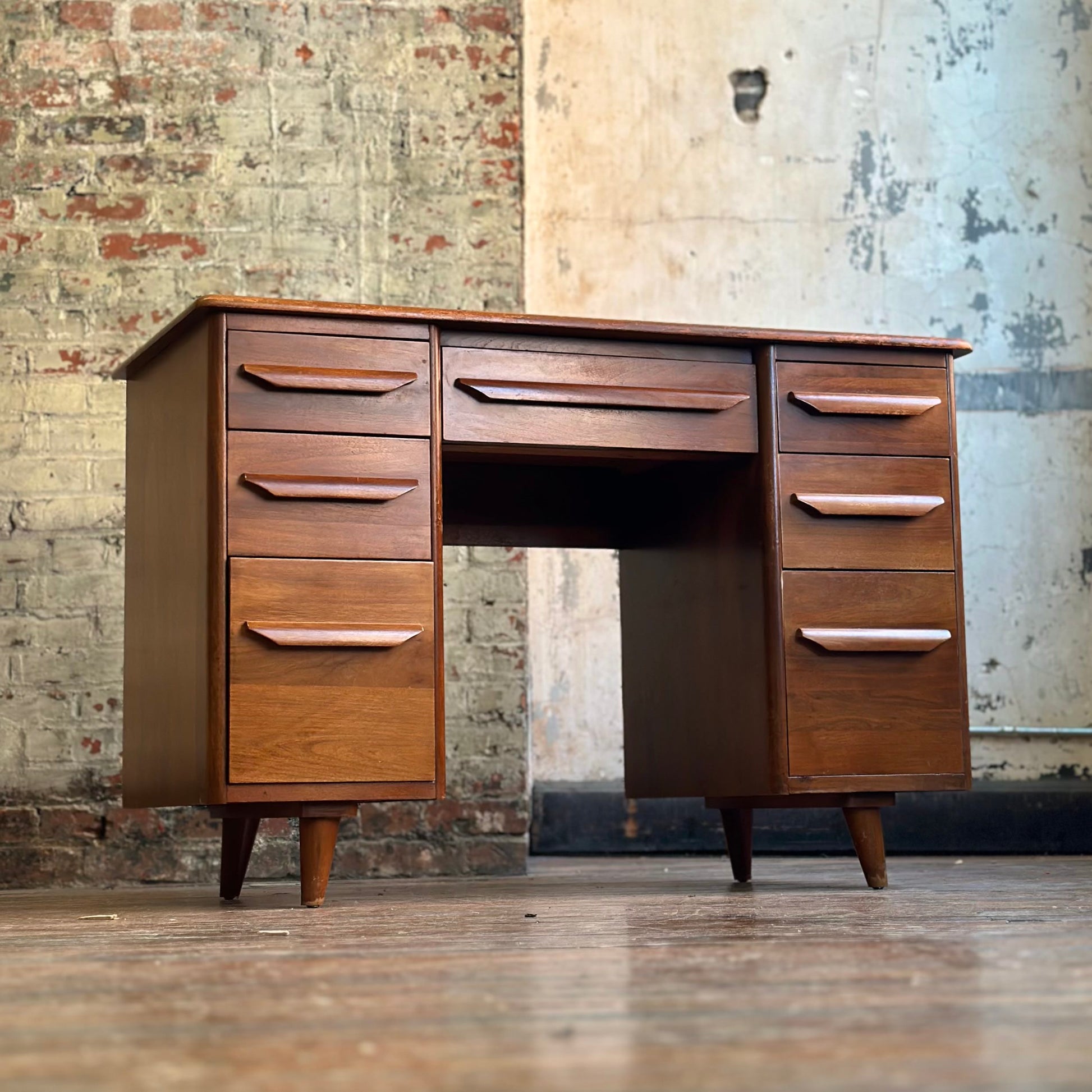 Wooden desk with multiple drawers against a textured wall.