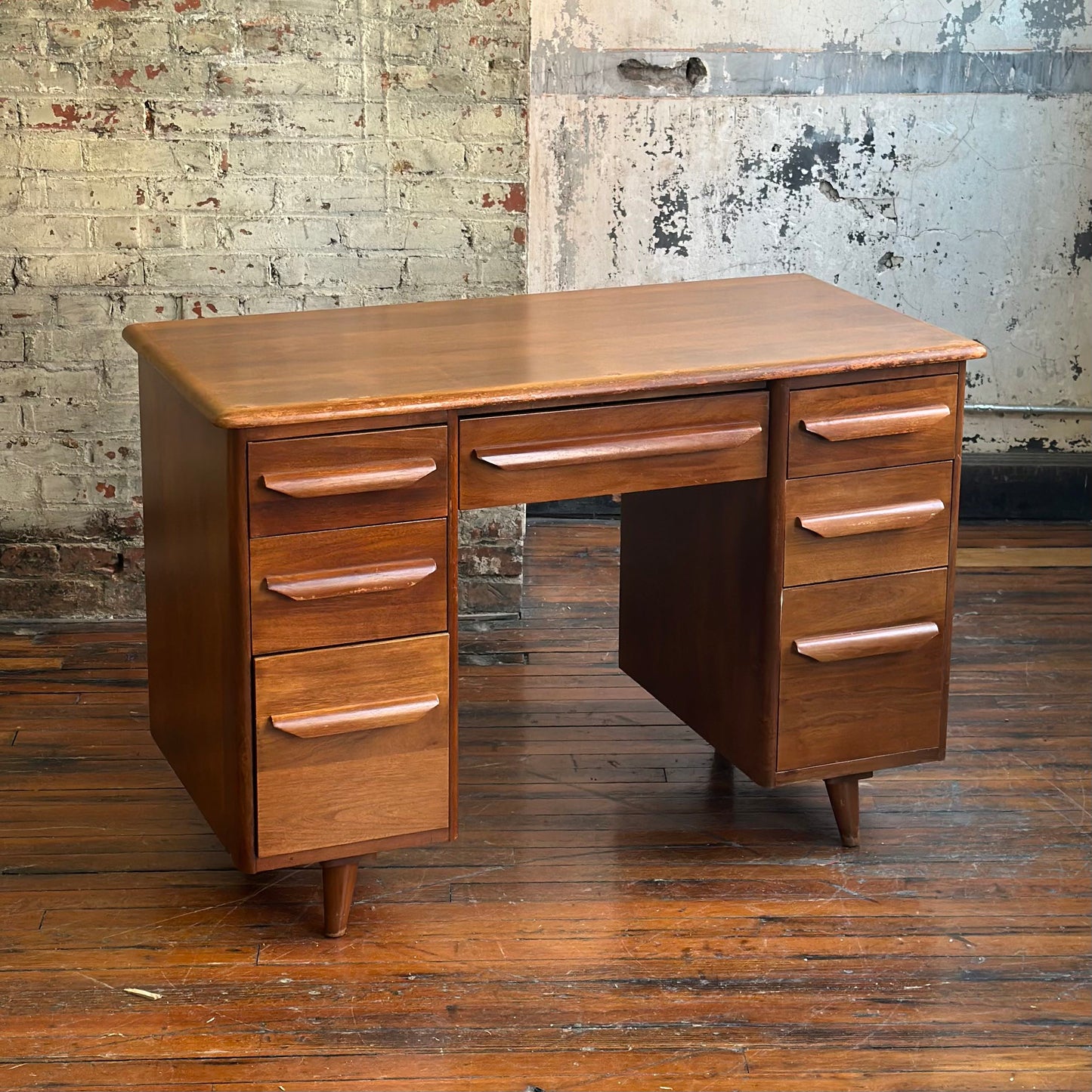 Wooden desk with multiple drawers against a textured wall.