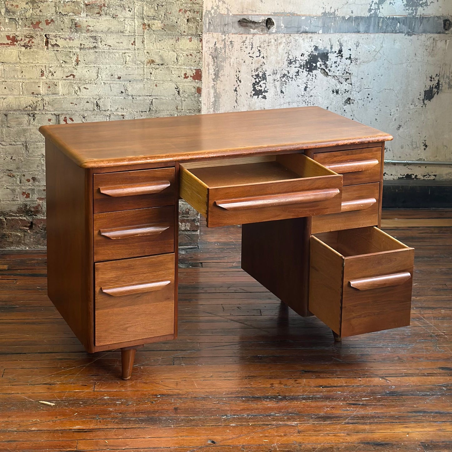 Wooden desk with multiple drawers against a textured wall.