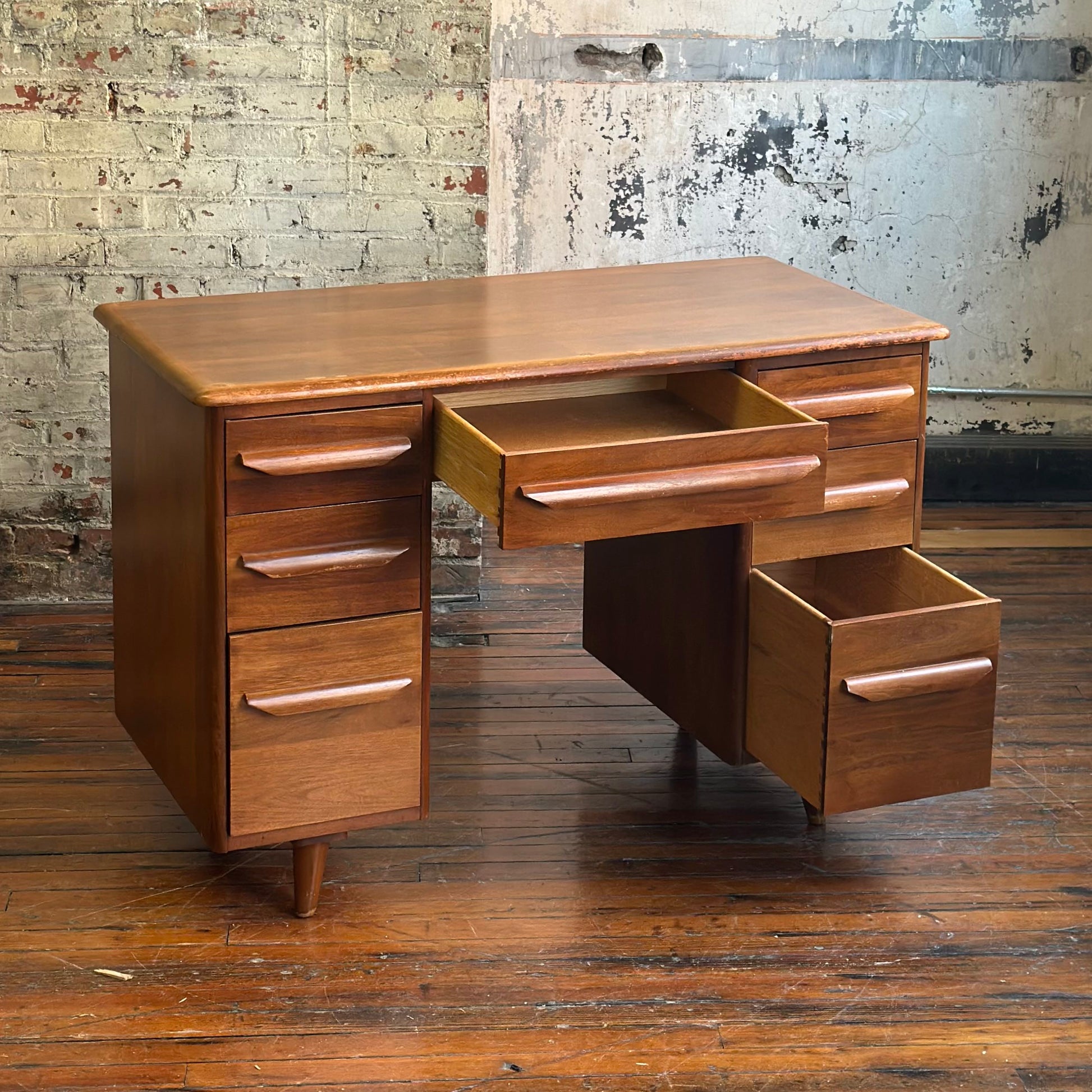 Wooden desk with multiple drawers against a textured wall.