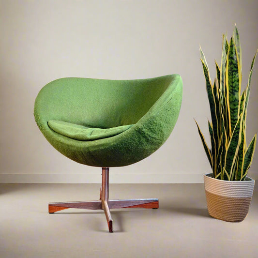 Green egg-shaped chair in a room with a brick wall and a potted plant.