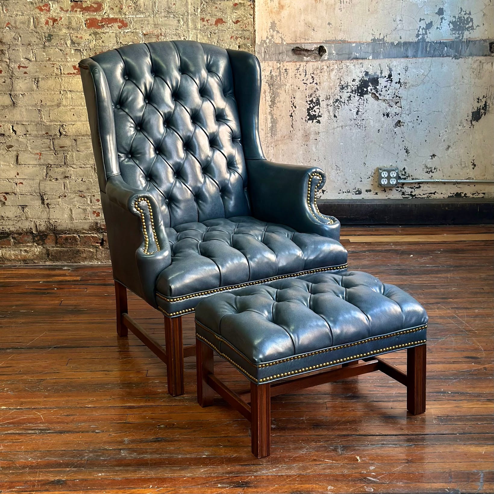 Blue leather armchair with matching ottoman on a wooden floor against a brick wall.