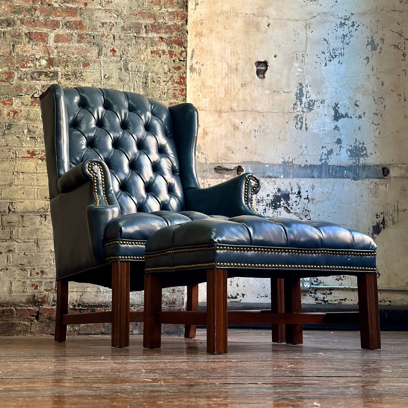 Vintage-style leather armchair with ottoman against a brick wall.